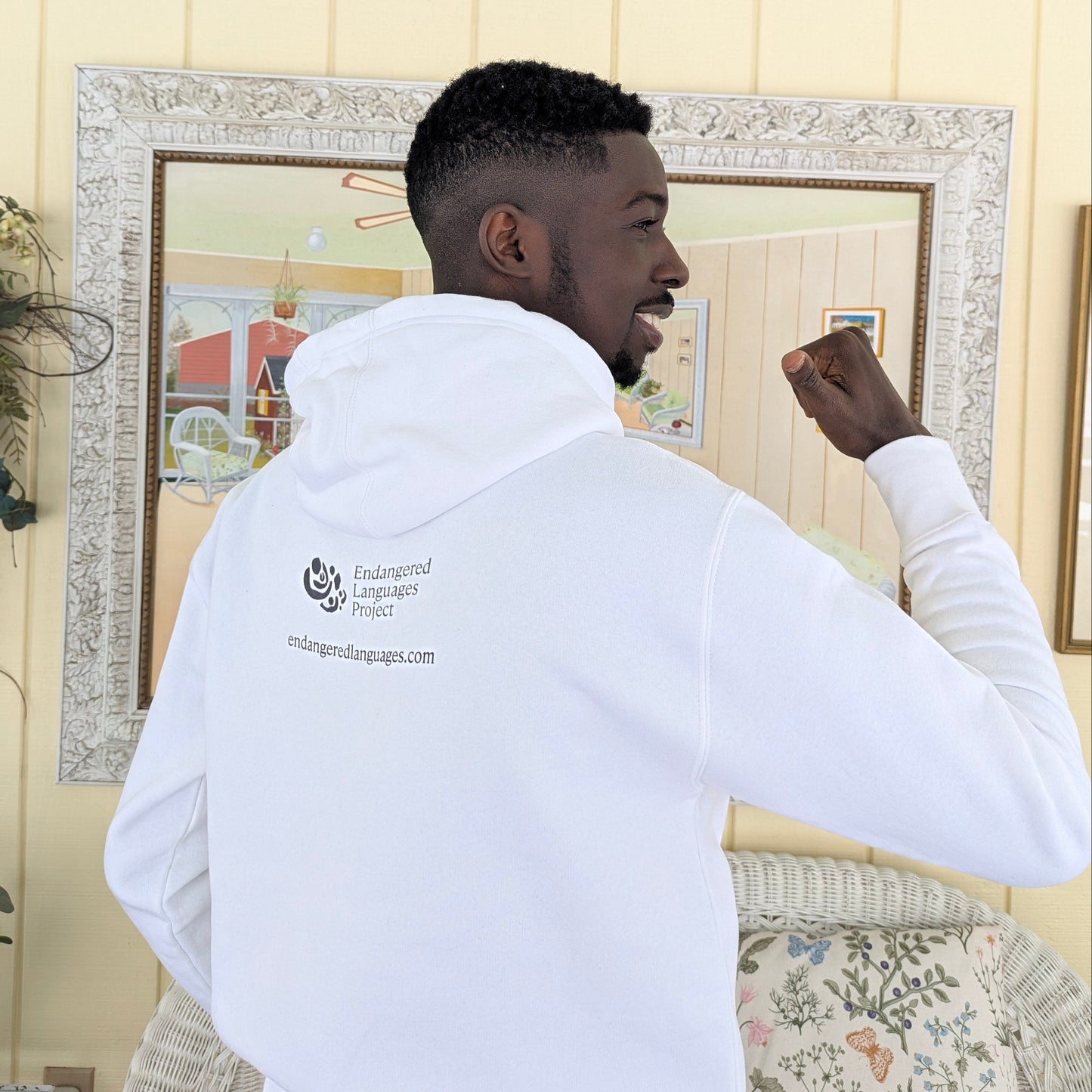 Young Nigerian man photographed from the back, wearing a white hoodie and pointing to the ELP logo on the back of the hoodie.